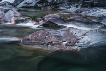 Atmosphärischer Naturhintergrund mit riesigen Steinen im Bergfluss. Große Felsen im mächtigen Wasserstrom, Nahaufnahme. Naturhintergrund mit Wald. Dunkel türkisblauer Fluss mit Steinen.