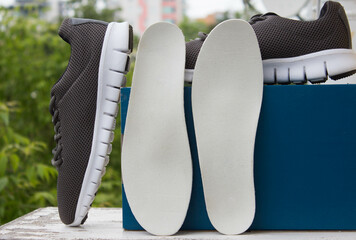 Leather orthopedic insoles in front of blue box and pair of sport shoes. Outdoors.