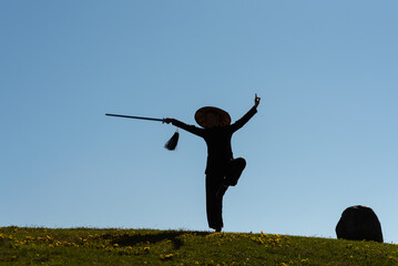 Asian woman with sword practicing taijiquan at sunset, chinese martial arts, healthy lifestyle concept.