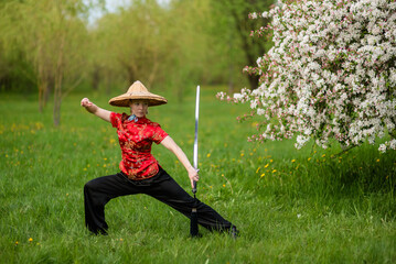 Asian woman with sword training with tai chi in the park, chinese martial arts, healthy lifestyle...