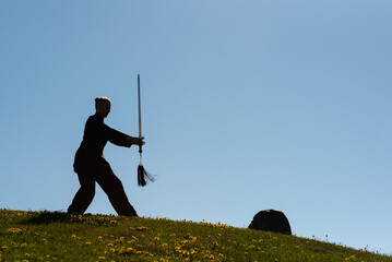 Asian woman with sword practicing taijiquan at sunset, chinese martial arts, healthy lifestyle concept.