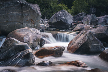 Atmosphärischer Naturhintergrund mit riesigen Steinen im Bergfluss. Große Felsen im mächtigen Wasserstrom, Nahaufnahme. Naturhintergrund mit Wald. Dunkel türkisblauer Fluss mit Steinen.