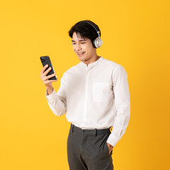 Young good looking asian man using smartphone and headphone listen to music isolated on yellow background