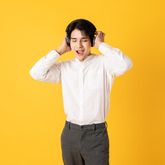 Young good looking asian man using smartphone and headphone listen to music isolated on yellow background