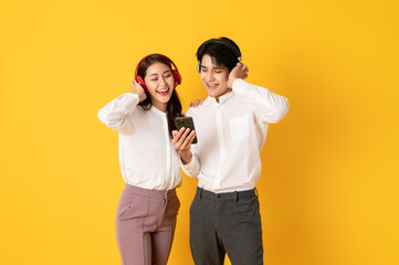 Two Young good looking asian couple using smartphone and headphone listen to music isolated on yellow background