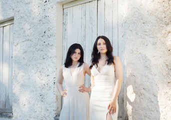 two young girls in white dress on background old white wall