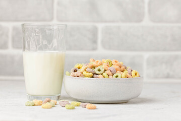 Easy breakfast whith fruit loops or fruit hoops  and a glass of milk. Colored flavored rings of cereals with milk on a white table.