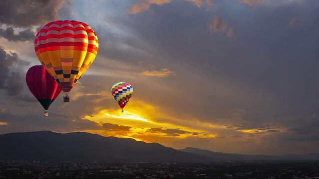 Multicolored hot air balloons floating against the orange sky over high mountain. aerial view.