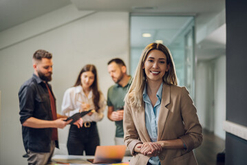 Obraz premium Businesswoman posing while having a meeting with her team in the office
