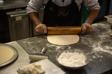 Fototapeta premium Male baker prepares bread. Male baker sprinkle the dough with flour. Making bread. Top view. Rustic style