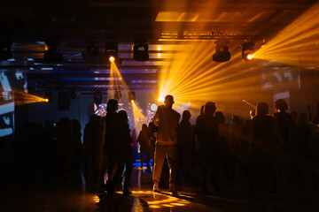 Corporate party event entertainment: yellow and blue spotlight or ray shines in the shadows of people silhouettes, loud music in the club, dancing, relaxing