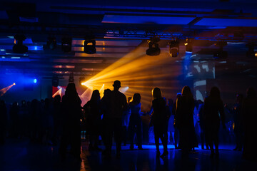 Corporate party event entertainment: yellow and blue spotlight or ray shines in the shadows of people silhouettes, loud music in the club, dancing, relaxing