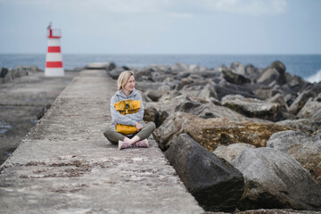 Obraz premium A woman sits with a backpack on an ocean pier.