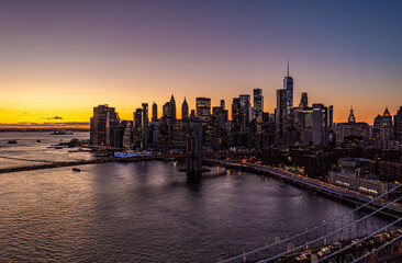 Lower Manhattan skyscrapers silhouettes against colourful sunset sky. Heavy traffic on roads along water. Manhattan, New York City, USA