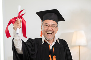 Asian elderly in cap and gown smile and celebration proud success graduate. Cheerful senior man...