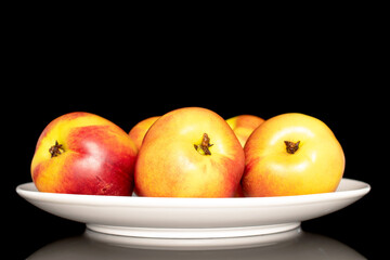 Several sweet organic nectarines on a ceramic plate, close-up isolated on a black background.