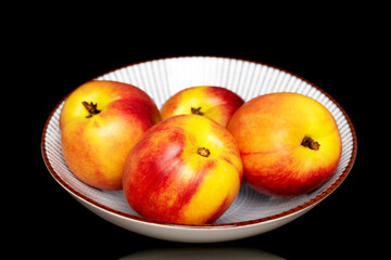 Several sweet organic nectarines on a ceramic plate, close-up isolated on a black background.
