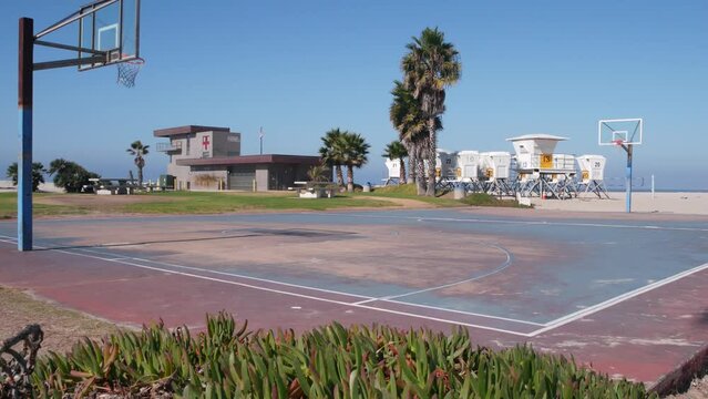Palm trees and basketball sport field or court on beach, California coast, USA. Streetball playground on shore and lifeguard stand, tower ot station. Mission beach, San Diego. Hoop, backboard and sky.