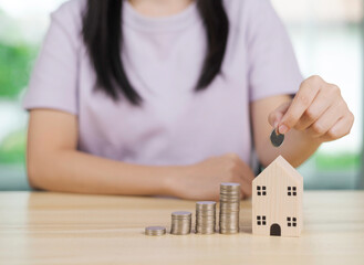 Young woman hand put money coins into a wooden house on the table for saving money for buying a house. financial concept ideas for saving money and loan concept.
