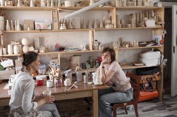 artisan girls are sitting at a table in a workshop producing wooden toys.