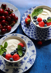 Natural yoghurt bowl close up photo. Sweet breakfast on blue stone table. Strawberry, blueberry, cherry, mint leaves on Greek yogurt. Eating healthy concept. 