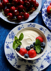 Natural yoghurt bowl close up photo. Sweet breakfast on blue stone table. Strawberry, blueberry, cherry, mint leaves on Greek yogurt. Eating healthy concept. 
