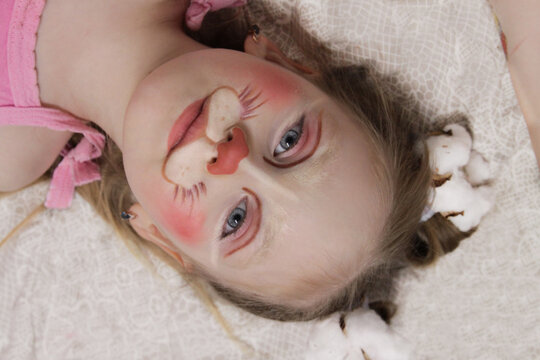 A girl with blue eyes and children's makeup. A child with a funny face painting. Makeup of a rabbit on the face of a child. Children's holiday, event, birthday, easter bunny, entertainment