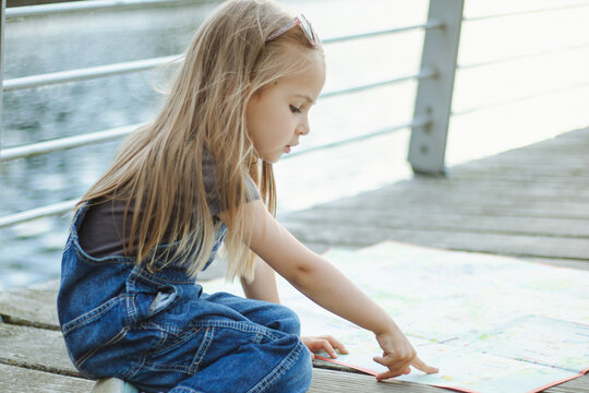 A child on the waterfront in jeans looks at a map of attractions