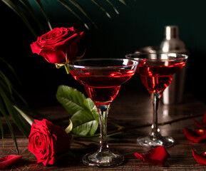 Delicious refreshing beverage drink red cocktail with red rose and petals on wooden table. Romantic, Valentines day concept.