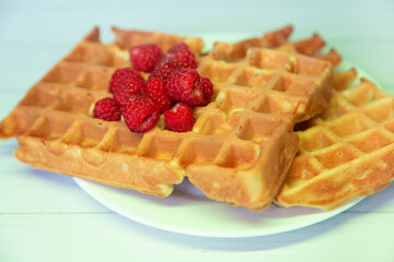 Front view on fresh breakfast. Heap of fresh gold fried viennese waffles with red raspberries on top lay on white plate. Selective focus