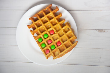 Colorful pink, yellow circle candies lay inside viennese waffle cell on white wooden table background. Kids breakfast, funny game. Top view, flat lay