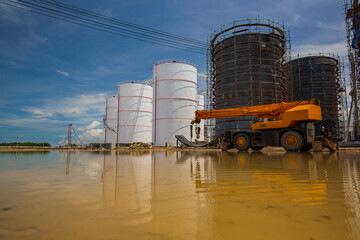 Obraz premium Constuction of an oil derrick crane, big oil tanks water background
