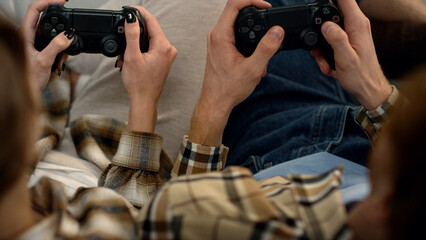 Players hands holding gamepads resting home closeup. Couple enjoy video game.