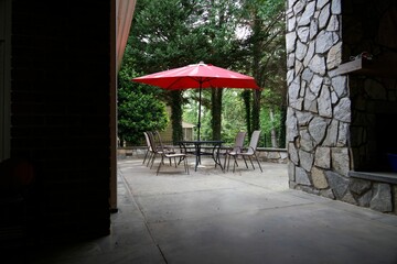 Red patio umbrella over an outdoor table and chairs on a background of green trees