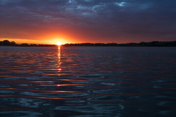 Wonderful colorful sunset on river. View of dramatic sky reflection on water and birds flying in the sky.