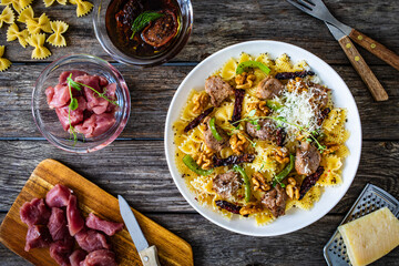 Farfalle with roasted pork loin, sauce, parmesan cheese, nuts and  green bell pepper served on wooden table
