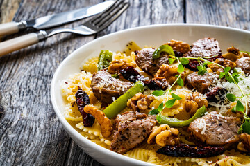 Farfalle with roasted pork loin, sauce, parmesan cheese, nuts and  green bell pepper served on wooden table
