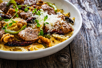 Farfalle with roasted pork loin, sauce, parmesan cheese, nuts and  green bell pepper served on wooden table
