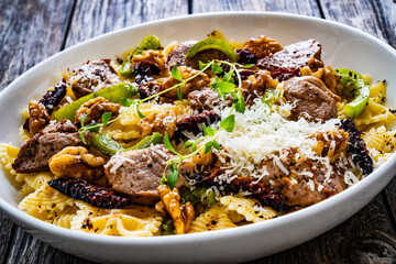 Farfalle with roasted pork loin, sauce, parmesan cheese, nuts and  green bell pepper served on wooden table
