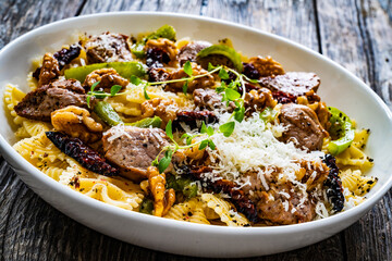 Farfalle with roasted pork loin, sauce, parmesan cheese, nuts and  green bell pepper served on wooden table
