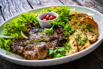 Roasted pork loin and fried potatoes with green vegetables  on wooden table

