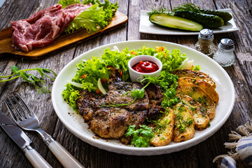 Roasted pork loin and fried potatoes with green vegetables  on wooden table
