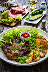 Roasted pork loin and fried potatoes with green vegetables  on wooden table
