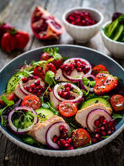 Tasty salad - roast pork loin, cucumber, cherry tomatoes, pomegranate, strawberries and fresh, green vegetables on wooden table
