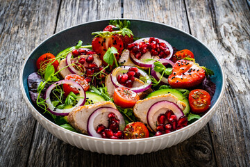 Tasty salad - roast pork loin, cucumber, cherry tomatoes, pomegranate, strawberries and fresh, green vegetables on wooden table
