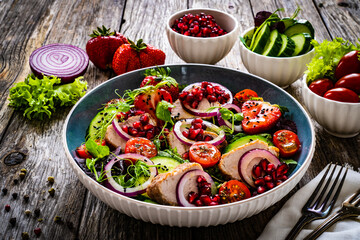 Tasty salad - roast pork loin, cucumber, cherry tomatoes, pomegranate, strawberries and fresh, green vegetables on wooden table

