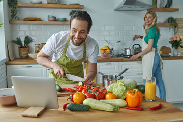 Happy man using digital tablet while cooking together with his girlfriend at the kitchen