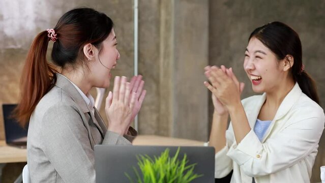 Two women showing joy and looking at data on their laptop, two business women looking at a monthly summary of sales that exceed sales targets and achieve profitable growth. Sales management concept