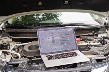 Computer diagnostics of the car in garage. Automotive mechanical technician using laptop computer programming and investing by car diagnostic software, car maintenance service concept
