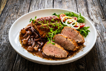 Roasted pork loin with shimeji mushrooms in sauce, fresh thyme, greens and cherry tomatoes on wooden table
